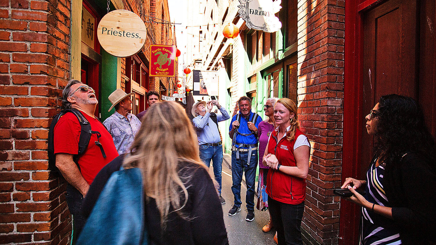 Group of people walking through a narrow alleyway with brick walls and street signs.