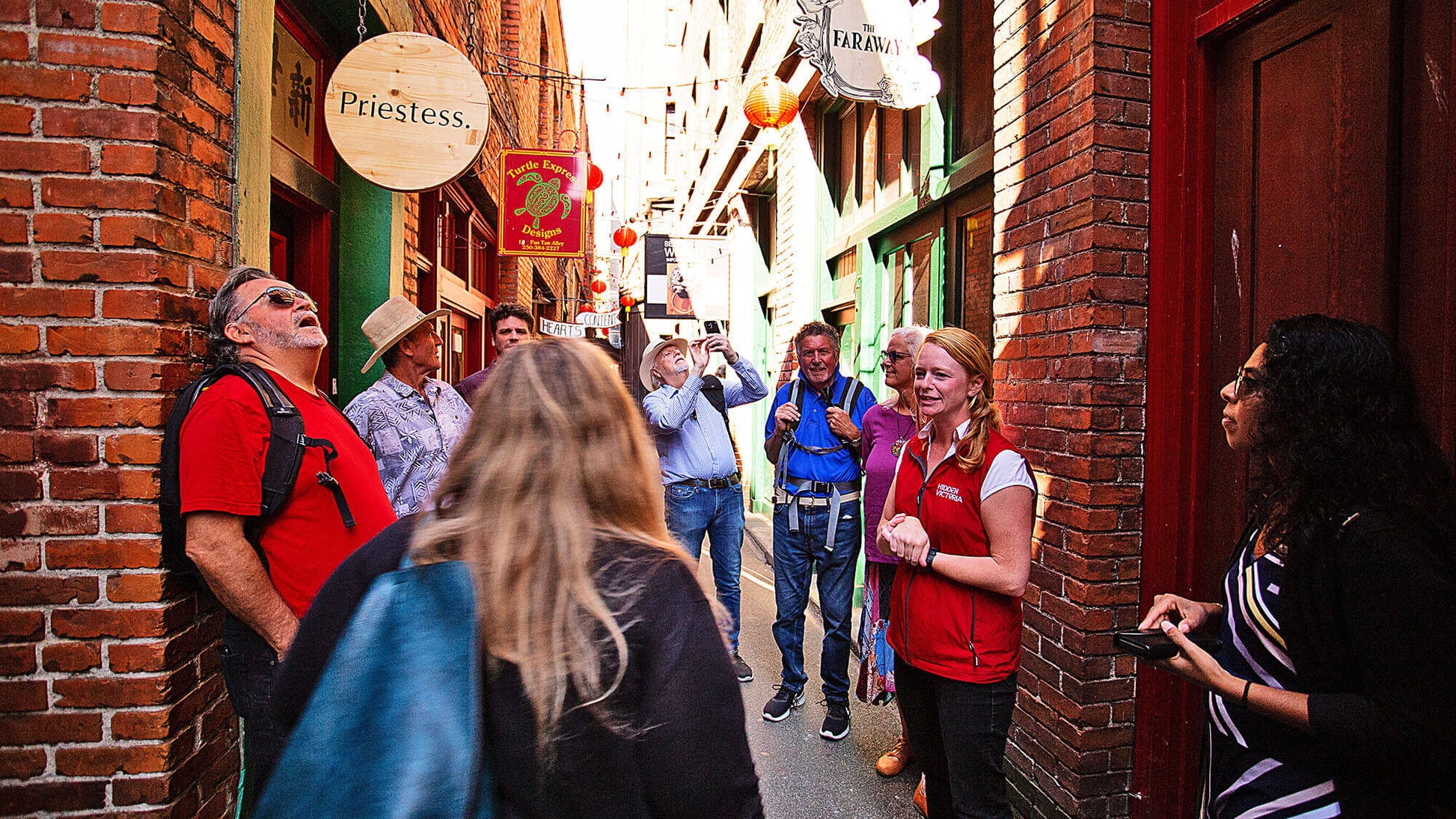 Group of people walking through a narrow alleyway with brick walls and street signs.